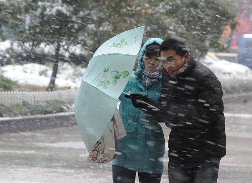 11月16日，两位南京市民在街头用雨伞遮挡风雪行走。从11月15日夜开始，南京市迎来罕见的早冬降雪，当地气象台发布暴雪蓝色预警信号。 新华社记者孙参摄